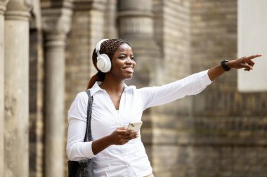 Akıllı telefonlu güzel bir Afrikalı kız şehri keşfediyor ve parmakla işaret ediyor..