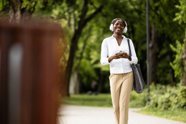 Güzel mutlu siyah kadın müzik dinliyor ve parkta yürüyor..