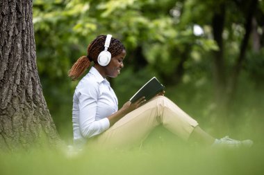 Güzel siyah kadın kitap okumayı ve açık havada müzik dinlemeyi sever..