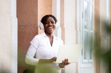 Güzel Afrikalı kadın dizüstü bilgisayarını tutuyor ve kameraya bakıyor..