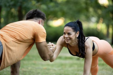 Spor salonundaki kadın, antrenörüyle parkta kalas egzersizi yapıyor..