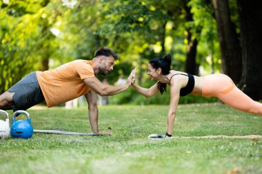 Fitness kadını ve kişisel antrenör kalas egzersizi yapıyor ve el ele tutuşuyorlar..