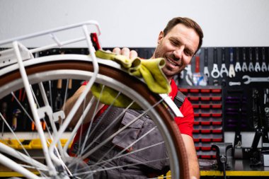 Arka tekerlek üzerinde çalışan deneyimli bir bisiklet tamircisi. Duvarda asılı duran arka plan araçlarında.