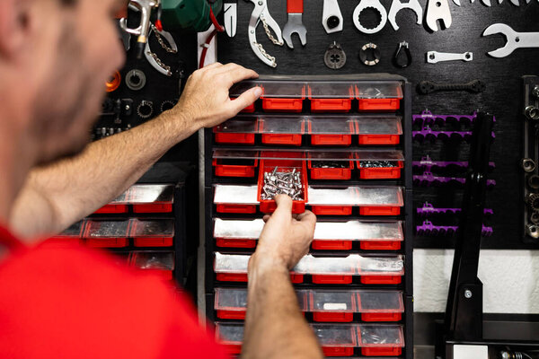 Professional serviceman or mechanic standing in front of the tool board and taking screws and bolts.