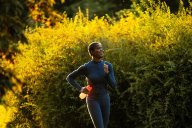 Gülümseyen siyah kadın su şişesiyle dışarıda koşuyor..