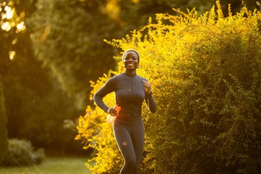 Gün batımında parkta koşan siyah bayan sporcu..