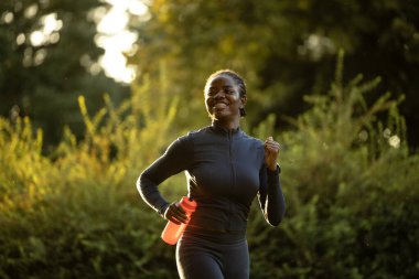 Gün batımında parkta koşan siyah bayan sporcu..