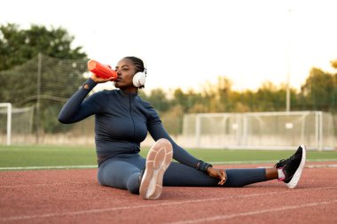 Siyah kadın koşucu ya da sporcu antrenmandan önce vücut çalışıp ısınıyor. Eğitimde su içen yüksek motivasyonlu bayan sporcu.
