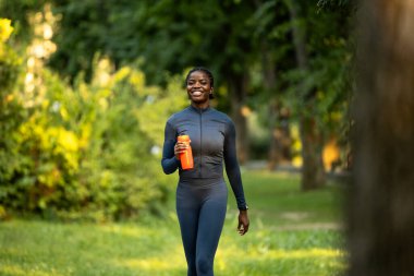 Gülümseyen siyah kadın su şişesiyle dışarıda koşuyor..