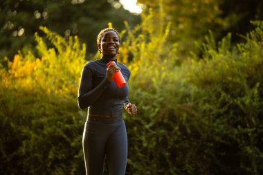 Gün batımında koşan siyah bir bayan sporcu. Siyah sporcu kadın gün batımında dışarıda antrenman yapıyor..