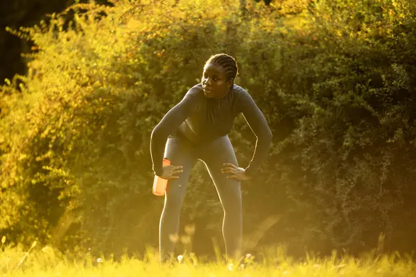 Gün batımında parkta koşan siyah bayan sporcu.