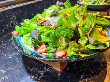 Farklı türde marul, dilimlenmiş çilek dilimlenmiş üzüm, gri tabakta fındık. Bir şenlik, parti ya da düğün organizasyonunda