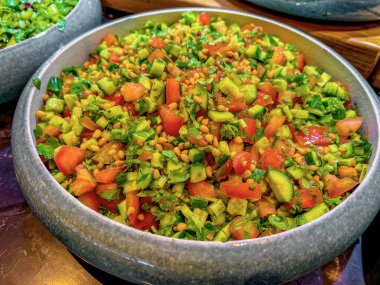 salad of tomatoes, cucumbers, parsley or cilantro and pine nuts with spicy sauce in a large gray dish. at catering event on some festive event, party or wedding. buffet