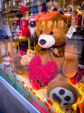 Budapest, Hungary - February 10, 2023. A large plush toy - a red bear with a pillow in the form of a heart sits in a shop window.