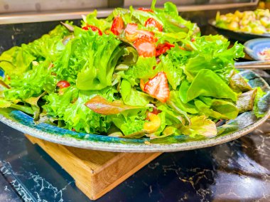 Farklı türde marul, dilimlenmiş çilek dilimlenmiş üzüm, gri tabakta fındık. Bir şenlik, parti ya da düğün organizasyonunda