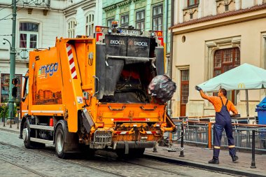 Krakow Polonya 8 Ağustos 2022: Şafak vakti çöp toplama, büyük siyah çöp torbası atan işçiyle birlikte turuncu araba çöp kamyonu. Temizliği ve düzeni korumak.