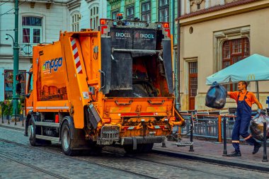 Krakow Polonya 8 Ağustos 2022: Şafak vakti çöp toplama, büyük siyah çöp torbası atan işçiyle birlikte turuncu araba çöp kamyonu. Temizliği ve düzeni korumak.