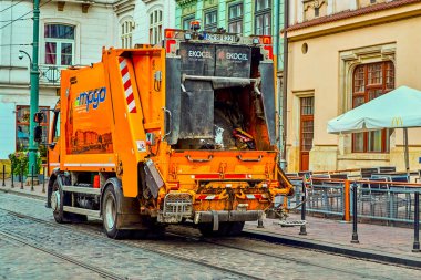 Krakow Polonya 8 Ağustos 2022: Şafak vakti çöp toplama, büyük siyah çöp torbası atan işçiyle birlikte turuncu araba çöp kamyonu. Temizliği ve düzeni korumak.