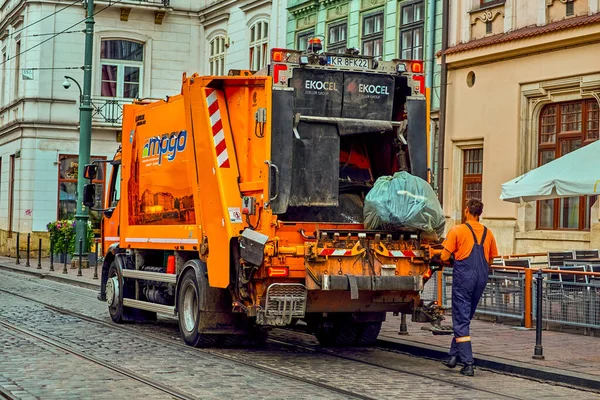 Krakow Polonya 8 Ağustos 2022: Şafak vakti çöp toplama, büyük siyah çöp torbası atan işçiyle birlikte turuncu araba çöp kamyonu. Temizliği ve düzeni korumak.