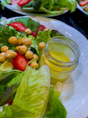 Farklı türde marul salatası, doğranmış çilek, fındık ve salata sosu beyaz tabakta cam bir kavanozda. Bir şenlik organizasyonunda, bir partide ya da düğünde, bir restoranda. Büfe yemek servisi.