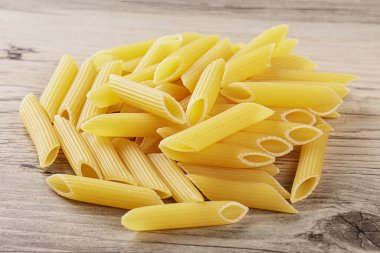 Çiğ Penne Rigate erişteleri gri ahşap arka planda izole edilmiş.