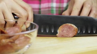 Mutfaktaki tahta kesme tahtasının üzerinde sosis kesen kadına yakın çekim.