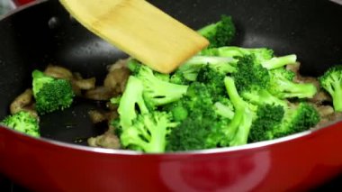 Kadın, mutfaktaki fırında domuz eti ve brokoliden oluşan lezzetli bir Çin yemeği pişiriyor.