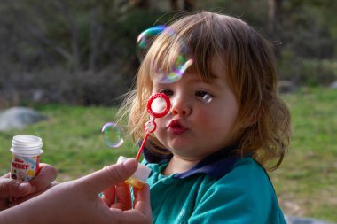 İki yaşında güzel bir sarışın kız güneşli bir günde sabun köpüğü üflüyor.