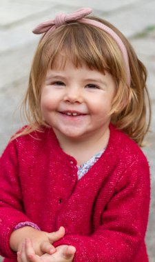 Kırmızı kazaklı gülümseyen kızın orta boy portresi.