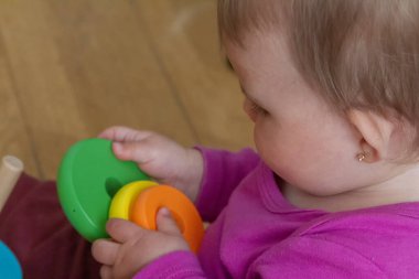 A one-year-old baby girl playing with colorful rings on the floor. clipart