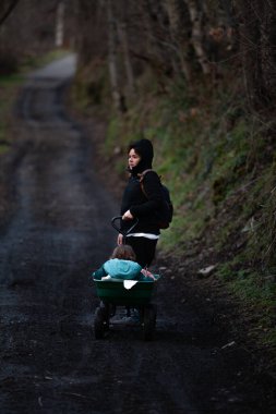  a mother pushing her daughter in a stroller on a tough mountain trail, emphasizing the effort and dedication of parenting in outdoor settings. clipart