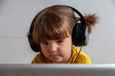 İki yaşında, sarı saçlı, büyük kulaklık takmış bir dizüstü bilgisayarın önünde oturmuş uzaktan kumanda simülasyonuyla oyun oynuyordu.. 