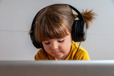 Güneş sarısı giyinmiş, örgülü saçları olan çekici bir genç kız, dizüstü bilgisayar kullanırken ve kulaklık takarken çok derinden odaklanmış görünüyor..