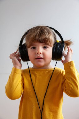 Müziğe dalmış, büyük kulaklıklar takmış, genç artistik merakı sembolize eden, güneşli bir elbise giymiş sevimli bir çocuk..