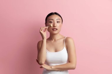 Yüz masajı. Cilt bakımı için Yeşim Yüz Kaykayı kullanan Asyalı Kadın, Pembe İzolasyon Arkaplanı 'nda Güzellik Tedavisi. Doğal Masaj Kapanışı Portresi Kullanan Kız 