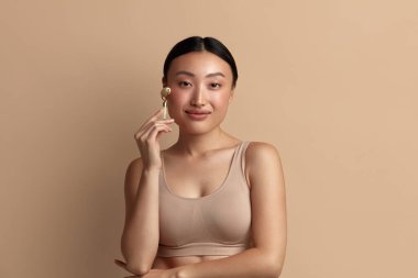 Yüz masajı. Cilt bakımı için Yeşim Yüz Pateni kullanan Gülümseyen Kadın, Bej Tecrit Arkaplan 'da Güzellik Tedavisi. Doğal Masaj Kapanışı Portresi ile Cilt Bakımı Yapan Kız 