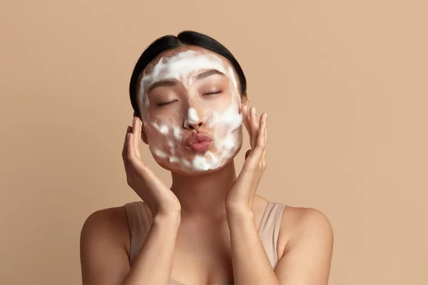 Face Skin Care. Funny Asian Woman Cleaning Facial Skin with Foam Soap. Happy Girl Cleansing Face Applying Facial Cleanser Closeup. High Resolution
