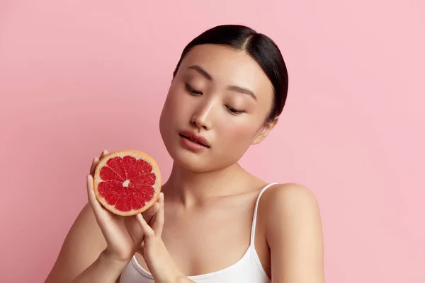 Beautiful Woman Smiling with Grapefruit. Positive Woman with Radiant Face Skin Portrait. Girl Model with Natural Makeup and Glowing Hydrated Skin. Vitamin C Cosmetics Concept