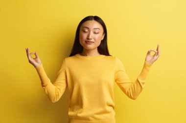 Huzurlu Kadın Stüdyoda Meditasyon. Asyalı Genç Kız 'ın portresi Rahatlama ve Meditasyon Hareketi Parmaklarıyla, Yoga Uygulaması. Kapalı Stüdyo Çekimi Sarı Arkaplanda İzole Edildi