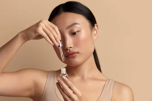 Woman Applying Serum on Face. Asian Girl Holding Essential Oil And On It. Beautiful Model Moisturizing Derma With Natural Vitamin E, Serum Collagen And Hyaluronic Acid