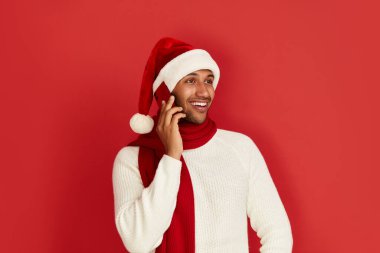 Akıllı Telefon Kullanan Mutlu Adam. Santa Hat 'taki çok ırklı adam gülümsüyor, cep telefonunu arıyor, sosyal medyada sohbet ediyor, mobil servisin tadını çıkarıyor. Reklam için Boş Kopya Alanı, Salon Stüdyosu Çekimi 