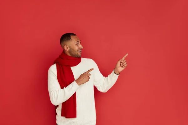 Smiling Man Pointing Hand. Positive Multiracial Guy Pointing Away Paying Your Attention at Empty Space for Advertisement. Indoor Studio Shot Isolated on Red Background