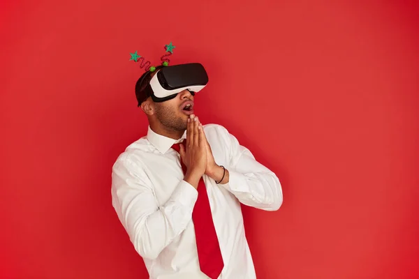 Focused Man Trying VR. Portrait of Amazed Multiracial Guy Discovering New Technologies Wearing Virtual Reality Headset, Futuristic 3d Vision. Indoor Studio Shot Isolated on Red Background