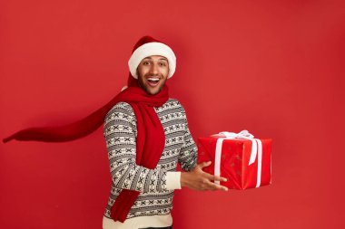 Happy Man Holding Hediyesi. Noel Baba Şapkalı Heyecanlı Adam Kırmızı Paketli Kutu 'da heyecanla bekliyor. Kapalı Stüdyo Çekimi Kırmızı Arkaplan 