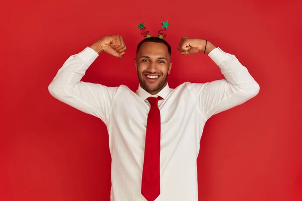 Multiracial Man Showing Biceps. Portrait of Confident Proud Man Showing Biceps, Feeling Power Success. Indoor Studio Shot Isolated on Red Background