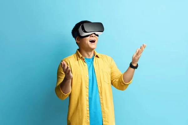 stock image Focused Man Trying VR. Portrait of Amazed Asian Guy Discovering New Technologies Wearing Virtual Reality Headset, Futuristic 3d Vision. Indoor Studio Shot Isolated on Blue Background 