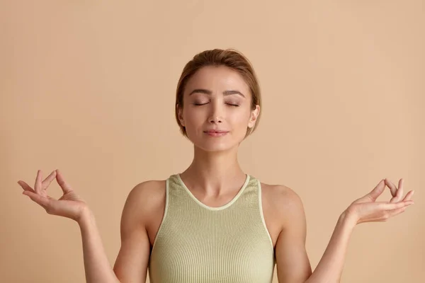 スタジオで瞑想する平和的な女性 魅力的な若い女の子の肖像指でリラックスして瞑想ジェスチャーを行う ヨガを練習 ベージュの背景に隔離された屋内スタジオショット — ストック写真