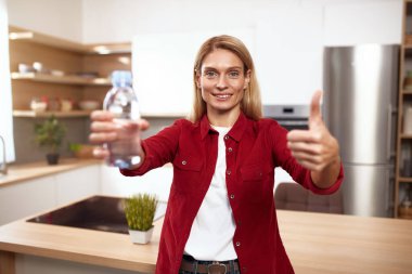 Su İçen Kıdemli Kadın. Mutfakta bir bardak taze suyla gülümseyen mutlu kadının portresi. Sağlık, Güzellik, Diyet ve Su Dengesi Konsepti