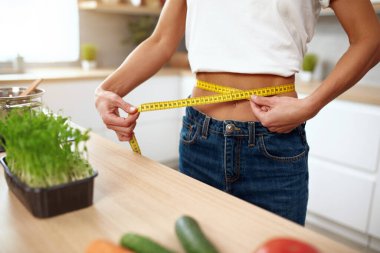 Yakından, Belini Ölçen Kadın. Mutfakta ölçü bandıyla diyet yapan kadının belini kesme görüntüsü. Diyet kavramı 