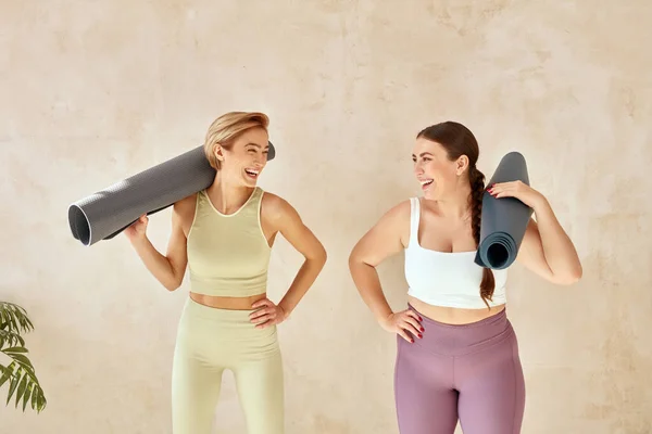 Laughing Women Posing After Yoga. Female Friends Laughing And Holding Yoga Mats After Yoga Session Together At Home. Attractive Girls In Sportswear Spending Free Leisure Time